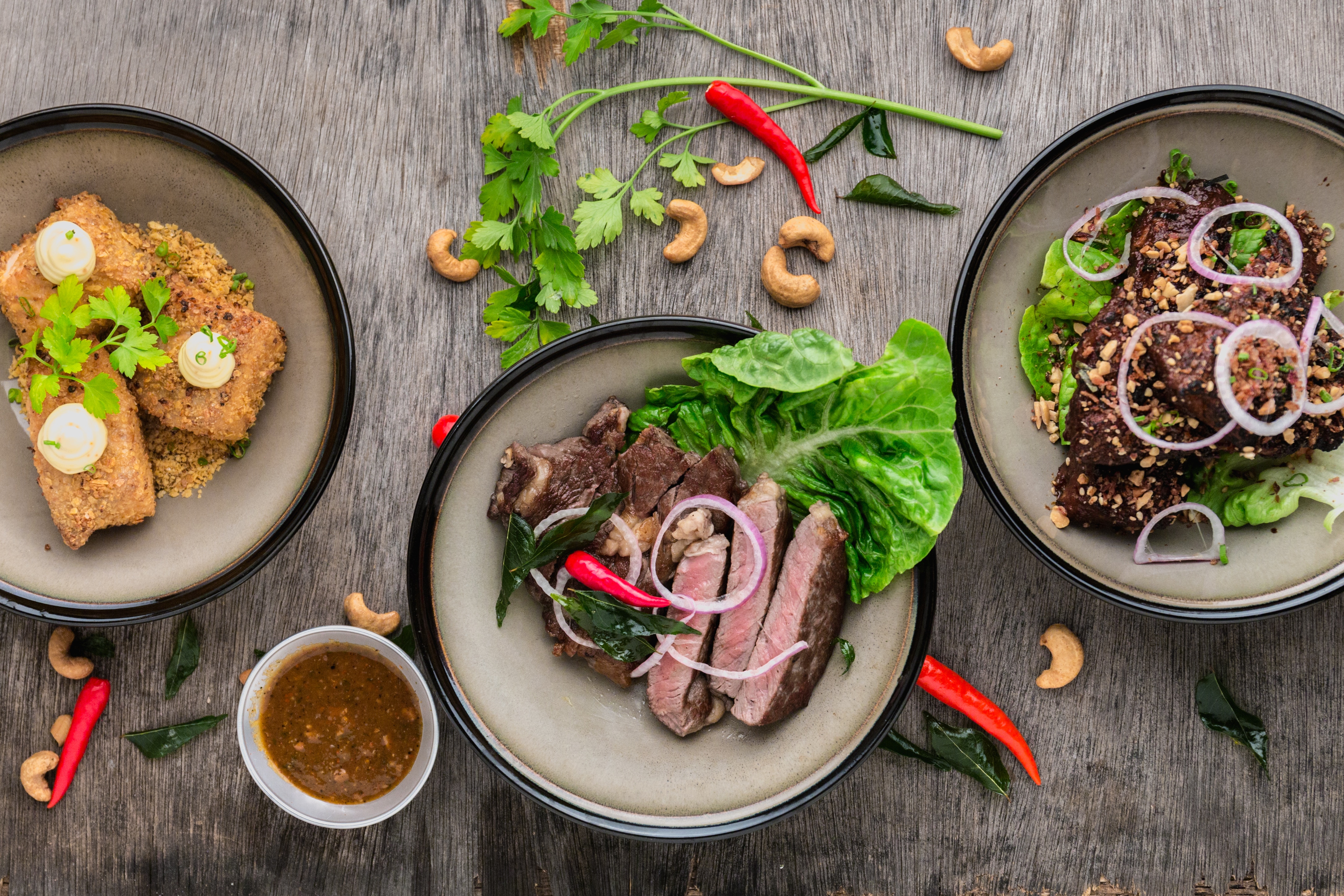 A spread of three rustic bowls, herb-flecked and freshly plated on weathered wood