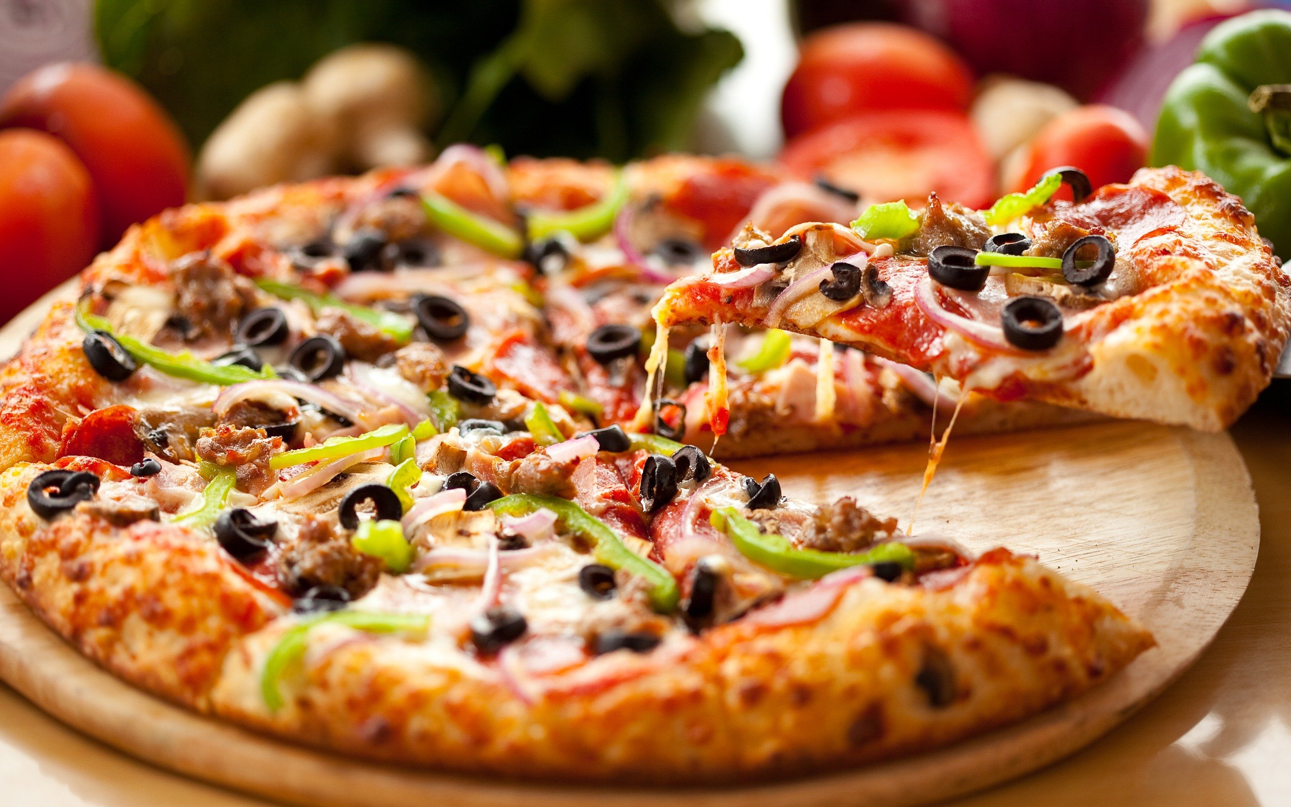 A loaded pizza with peppers, olives and herbs, a slice pulled away