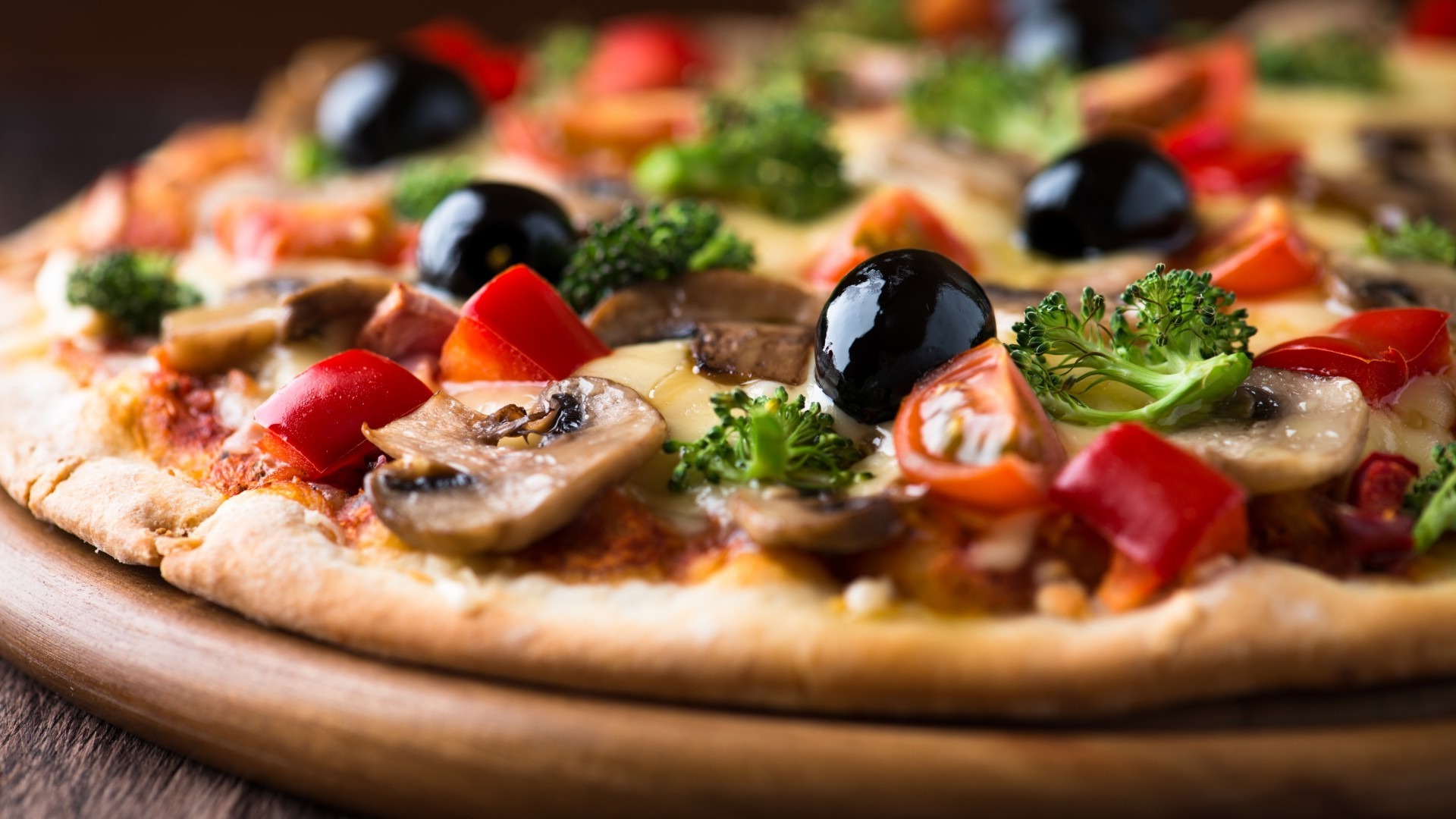 A wood-fired pizza with mushrooms, olives and peppers on a board
